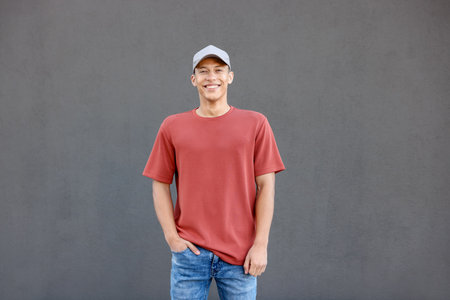 Young man wearing blank red t-shirt near gray wall. Mockup for designの写真素材