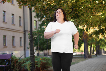 Smiling overweight woman running outdoors, low angle view. Space for textの写真素材