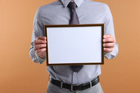 Man with blank frame on pale orange background, closeup. Mockup for designの写真素材