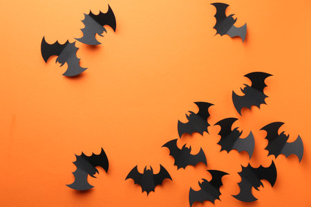Halloween decor. Black paper bats on orange background, flat lay. Space for textの写真素材