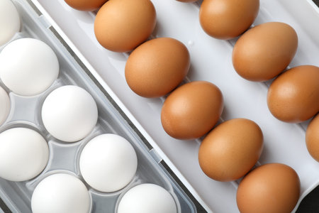 Raw chicken eggs in plastic containers on table, flat lay
