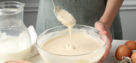 Woman making batter (liquid dough) at white table indoors, closeup