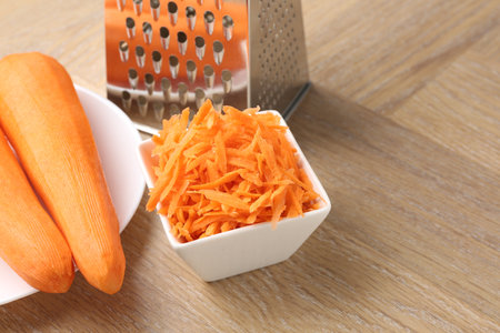 Whole and grater carrots and grater on wooden table, closeup. Space for textの写真素材