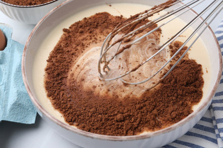 Adding cocoa powder into bowl with dough at white table, closeupの写真素材