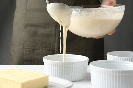 Woman pouring batter (liquid dough) into baking dishes at table indoors, closeupの写真素材