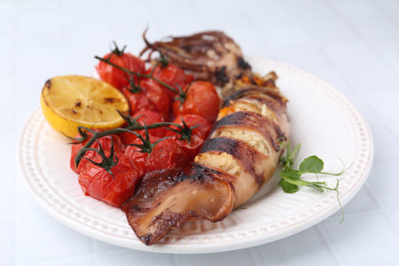 Tasty stuffed squid, microgreens, lemon and tomatoes on white tiled table, closeupの写真素材