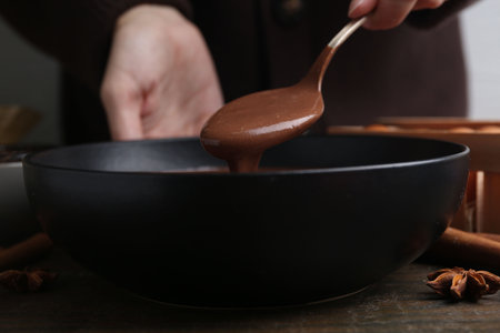 Woman mixing liquid chocolate dough with spoon in bowl at wooden table, closeupの写真素材