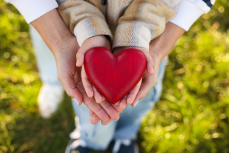 Mother with her son holding red wooden heart together outdoors, above view. Family bondingの写真素材