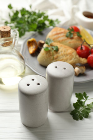 Shakers, parsley, pieces of tasty grilled squid, tomatoes and mushrooms on white wooden table, closeupの写真素材