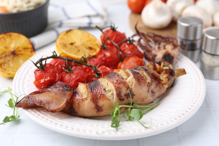 Tasty stuffed squid, microgreens, lemon and tomatoes on white tiled table, closeupの写真素材
