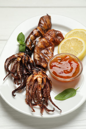 Tasty cooked squids served with lemon, sauce and basil on white wooden table, closeup
