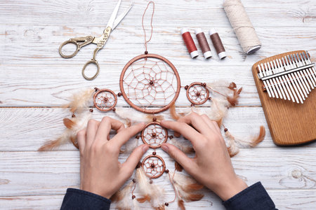 Woman making beautiful dream catcher at light wooden table, top viewの写真素材