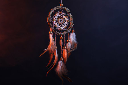 Beautiful dreamcatcher hanging in color lights against dark backgroundの写真素材