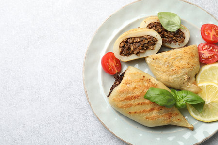 Pieces of tasty grilled squid stuffed with mushrooms, basil, tomatoes and lemon on light gray textured table, top view. Space for textの写真素材