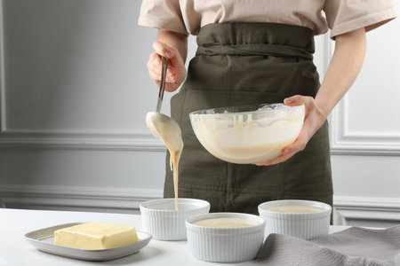 Woman pouring batter (liquid dough) into baking dishes at table indoors, closeupの写真素材