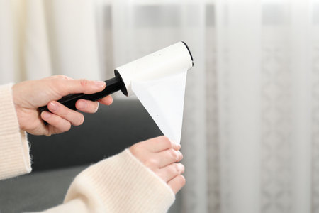 Woman removing sticky tape from lint roller at home. Space for text