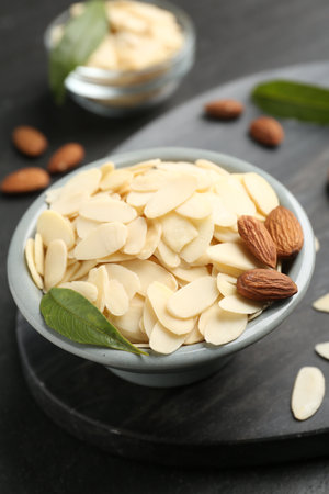 Fresh almond flakes, whole nuts and green leaf in bowl on gray table, closeupの写真素材
