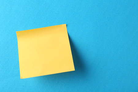 Blank yellow note on blue background, top view. Space for text