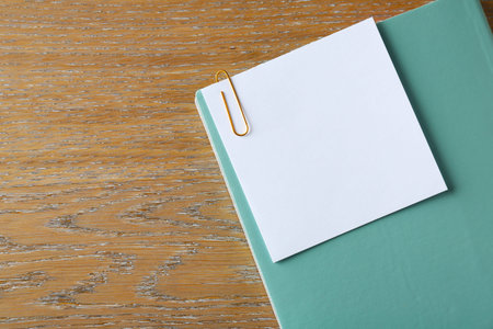 Blank note with clip and notebook on wooden table, top view. Space for text