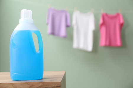 Bottle of laundry detergent on wooden table and hanging clothes against pale dusty green background, space for textの写真素材