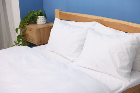 Bed with cozy fresh lines and nightstand near blue wall indoors