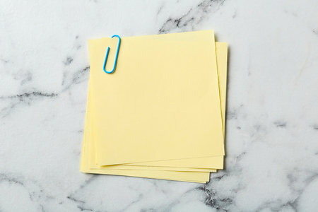 Blank yellow notes with paper clip on white marble table, top view. Space for textの写真素材