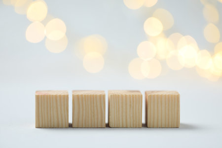 Blank wooden cubes on light background with blurred lights, space for text. Bokeh effect