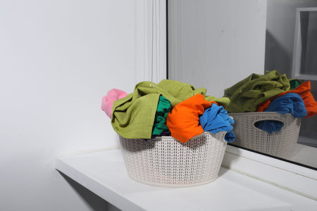 Laundry basket full of clothes on windowsill indoors