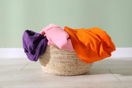 Laundry basket full of clothes on floor near light green wall