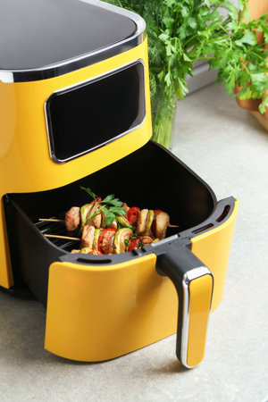 Air fryer with tasty chicken skewers on light countertopの写真素材