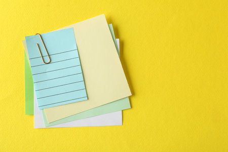 Blank colorful notes with paper clip on yellow background, top view. Space for text