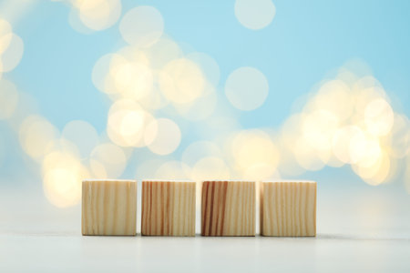Blank wooden cubes on white table against light blue background with blurred lights, space for text. Bokeh effectの写真素材