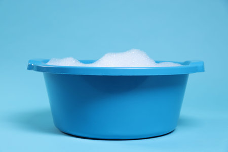 Plastic basin with soapy water on light blue background, closeupの写真素材