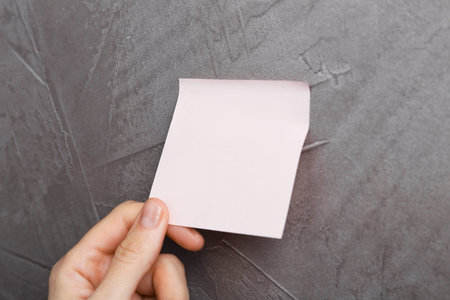 Woman putting blank adhesive note onto gray wall, closeup. Space for textの写真素材