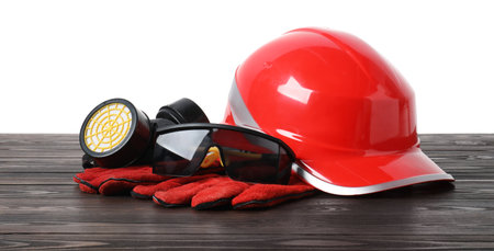 Safety equipment. Hard hat, respirator, protective gloves and goggles on wooden table against white backgroundの写真素材