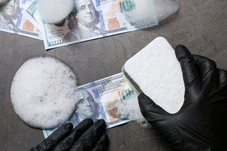 Money laundering. Man washing dollar banknotes with sponge and foam at black table, top viewの写真素材