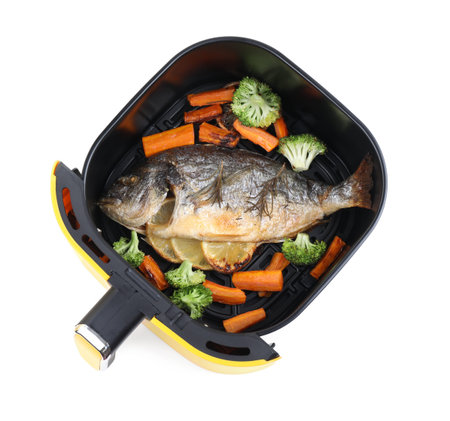 Cooked fish, lemon and vegetables in air fryer isolated on white, top view