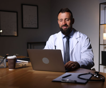 Doctor working on laptop at table in clinic during night shiftの写真素材