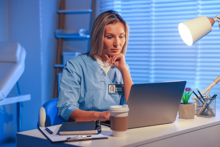 Doctor working on laptop at table in clinic during night shiftの写真素材