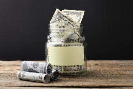 Jar with blank note and money on wooden table against black backgroundの写真素材