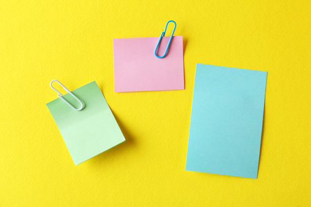 Blank colorful notes with paper clips on yellow background, flat lay. Space for textの写真素材
