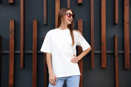 Young woman wearing blank white t-shirt near wall. Mockup for design
