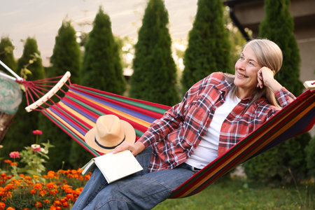 Senior woman with book resting in hammock outdoorsの写真素材