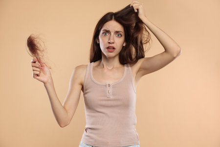 Woman with brush and lost hair on beige background. Alopecia problemの写真素材