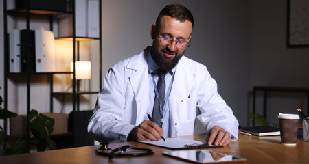 Doctor writing notes at table in clinic during night shiftの写真素材