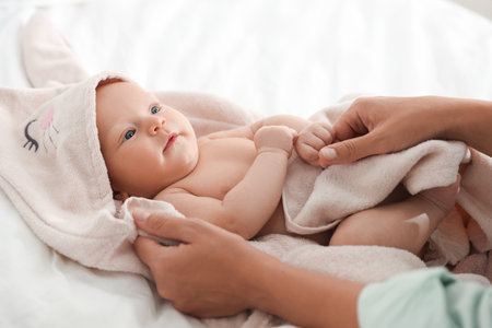 Mother covering her baby with towel after bathing on bed, closeupの写真素材