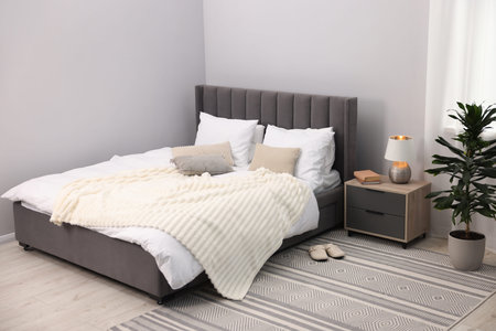 Large bed with lines, nightstand and houseplant near gray wall in bedroom. Interior design