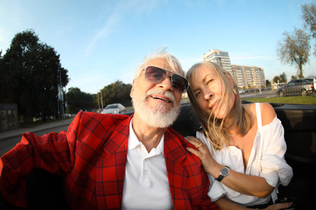 Senior couple enjoying cabriolet ride in city, wide angle lensの写真素材