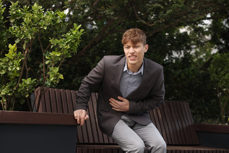 Young man in suit suffering from stomach ache and nausea outdoors