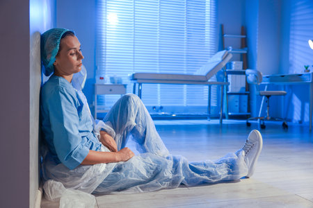 Tired doctor sitting on floor near wall in clinic during night shiftの写真素材